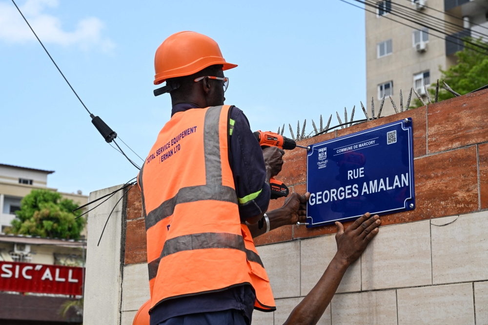 Workers mount the news signs of Georges Amalan street in Abidjan on April 16, 2025.  — AFP pic