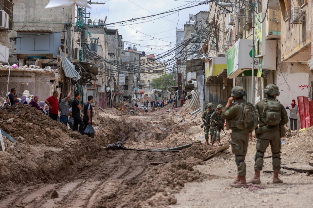 Israeli soldiers look on as Palestinians carry their belongings after being ordered to leave their homes during an Israeli operation in the Tulkarem camp for refugees in the northwest of the occupied West Bank May 2, 2025. — AFP pic