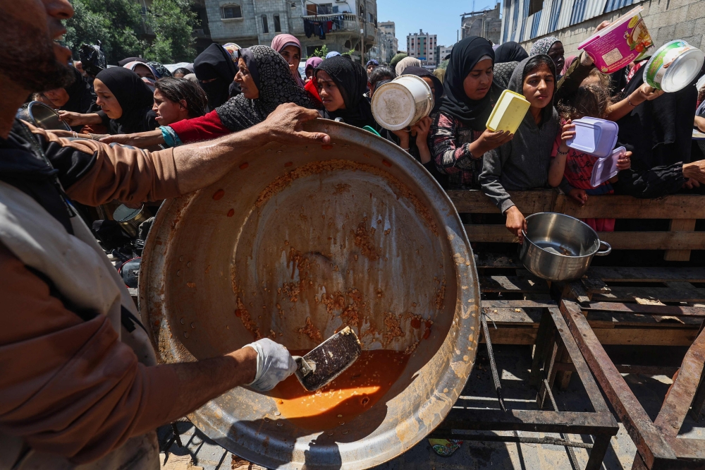 Palestinians queue for a portion of hot food distributed by a charity kitchen at the Nuseirat refugee camp in the central Gaza Strip on May 5, 2025. — AFP pic