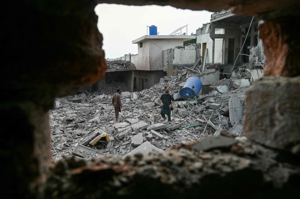 Locals stand on the debris of structures destroyed by Indian missile strikes, at the Government Health and Educational complex in Muridke about 30 kilometres from Lahore yesterday. — AFP pic