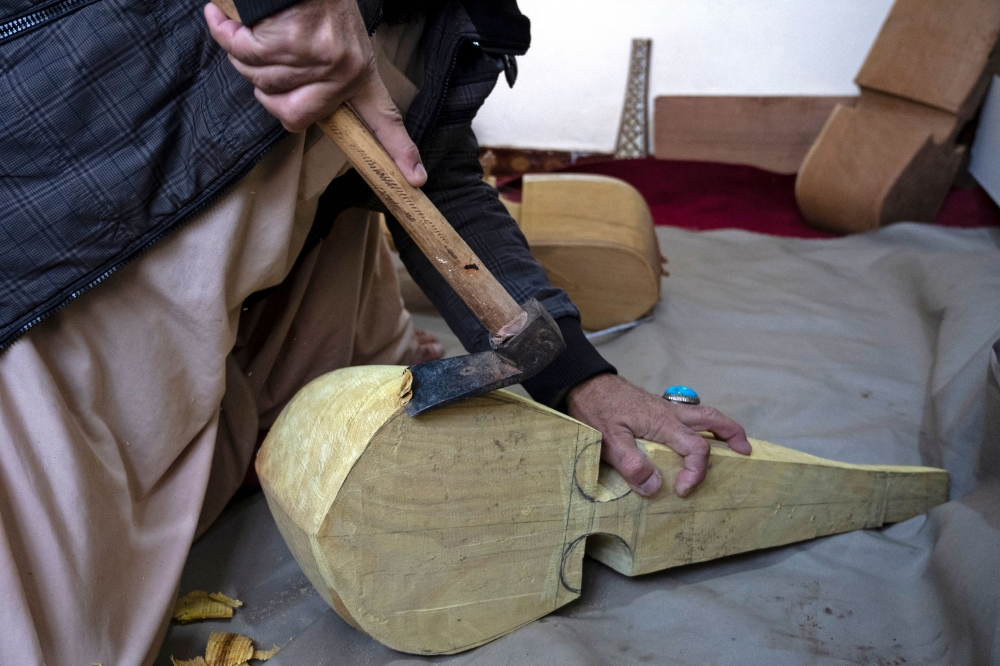 In this photograph taken on December 22, 2024, an Afghan craftsman Sakhi uses a hatchet as he makes Rubab, a string instrument of dried mulberry wood from deserts, at a workshop in Herat even amidst a Taliban crackdown on music. — AFP pic