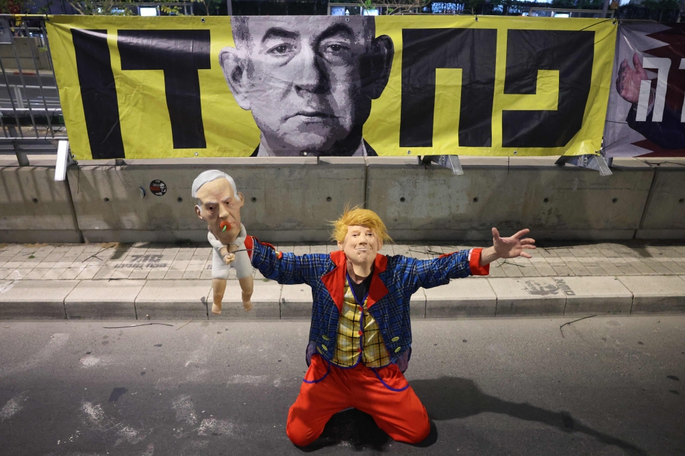 A demonstrator wearing a mask representing US President Donald Trump and carrying a doll with a mask depicting Israeli Premier Benjamin Netanyahu attends an anti-government protest calling for the end of the war and for action to secure the release of Israeli hostages held in the Gaza Strip since the October 7, 2023 attacks by Hamas, in front of the Israeli Defence Ministry in Tel Aviv on May 10, 2025. — AFP pic 