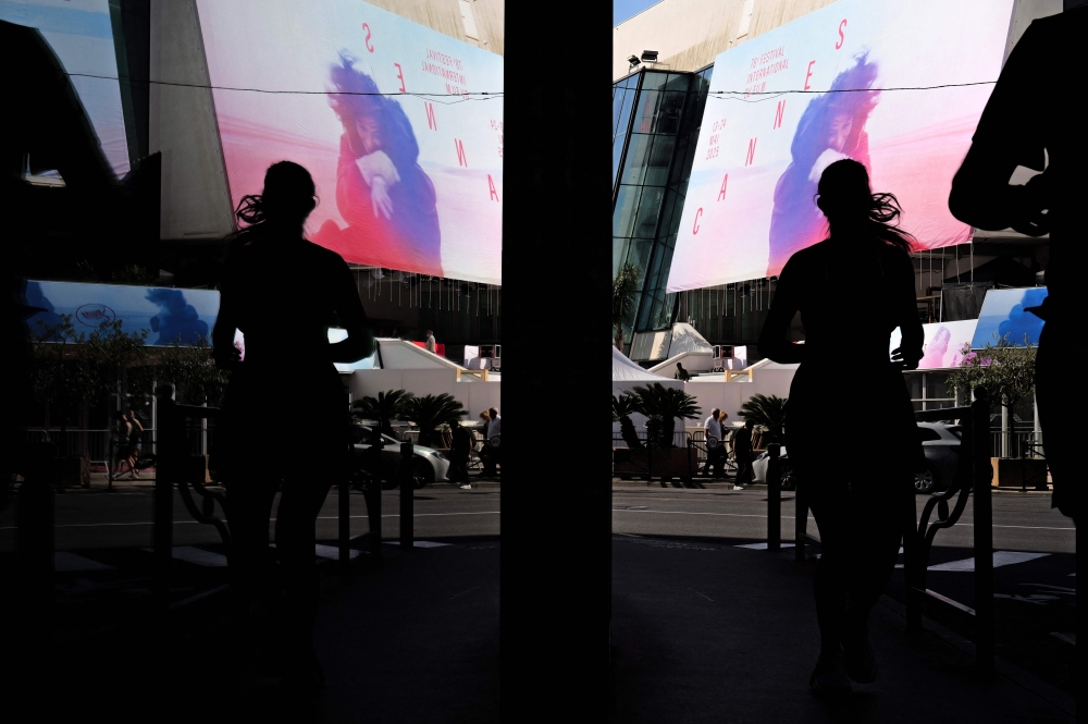 A woman runs past the poster of the 78th Cannes Film Festival installed on the facade of the Palais des Festivals in Cannes, south-eastern France, May 11, 2025. The 78th Cannes Film Festival will take place from May 13 to May 24, 2025. — AFP pic