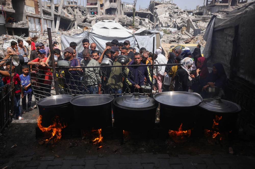 Palestinians queue to get a portion of cooked food from a charity kitchen in Jabalia in the northern Gaza Strip on May 17, 2025. — AFP pic