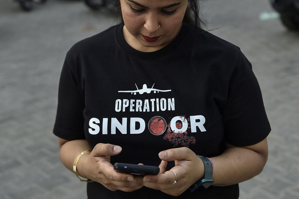 A woman wearing a T-shirt featuring 'OPERATION SINDOOR' checks her mobile phone near a market area in Ludhiana on May 17, 2025. — AFP pic