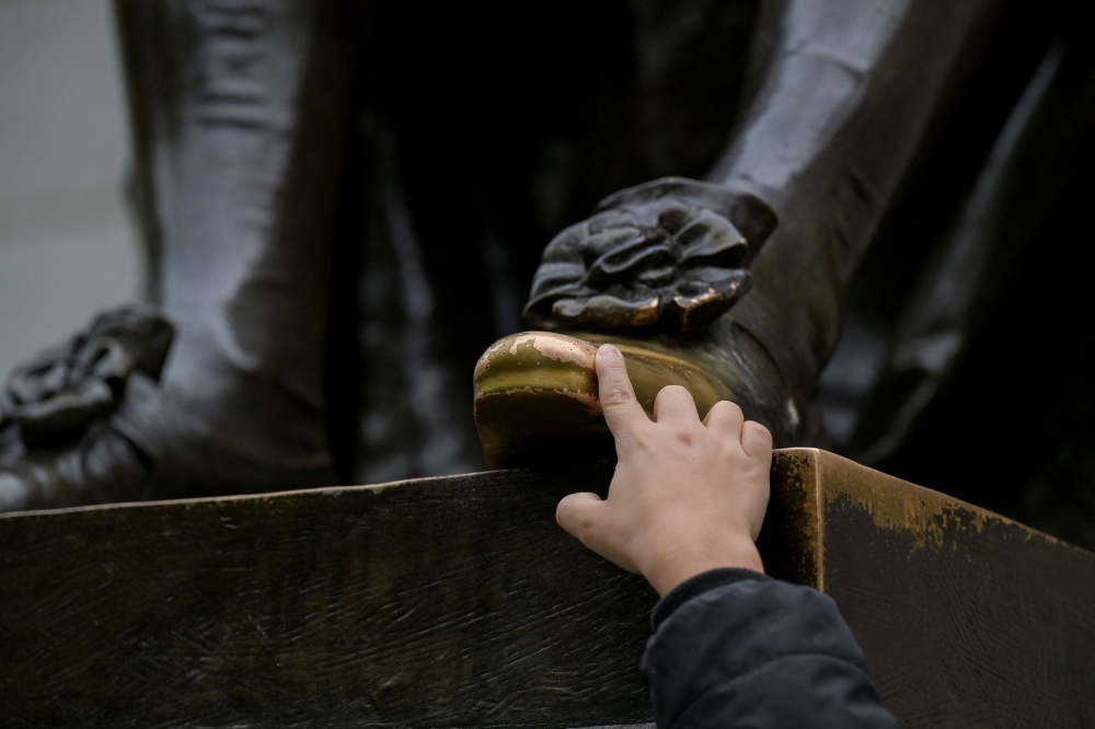 A boy touches the foot of the John Harvard statue on the campus of Harvard University in Cambridge, Massachusetts, May 23, 2025. — Reuters pic