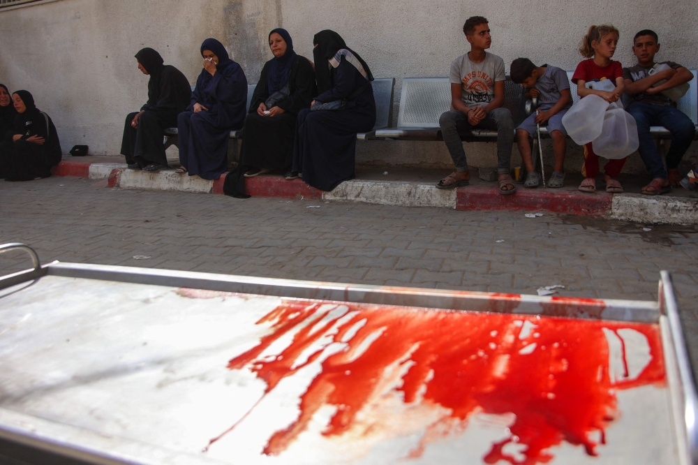 Palestinians mourn relatives killed in an Israeli strike as they sit next to a blood-stained gurney at Al-Shifa hospital in Gaza City on May 18, 2025. — AFP pic