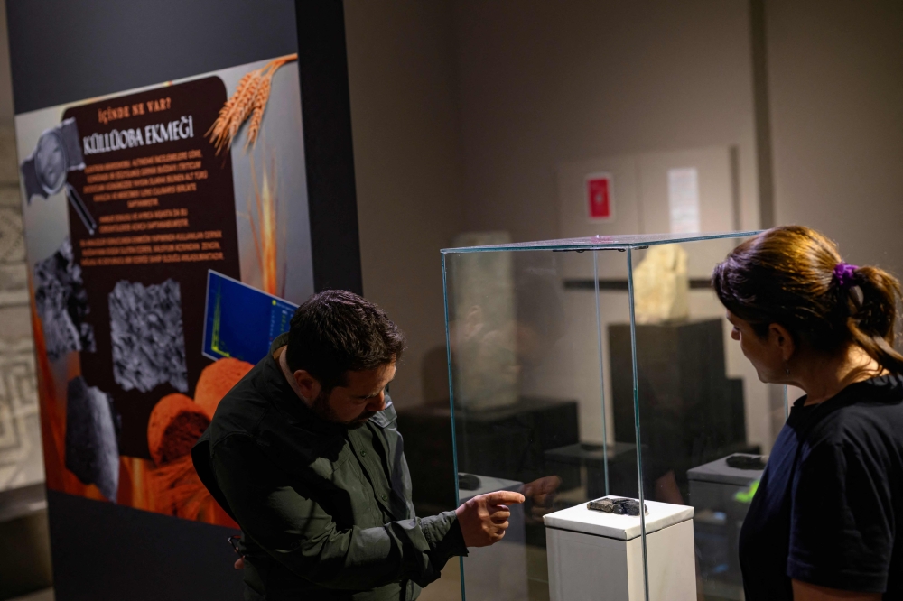 Archeologists Murat Turkteki (left) and Deniz Sari look at Kulluoba bread, a 5,000 years old bread unearthed in an archeological excavation in Eskisehir province, in central Turkiye, and exhibited at Eskisehir ETI archeology museum, May 23, 2025. — AFP pic