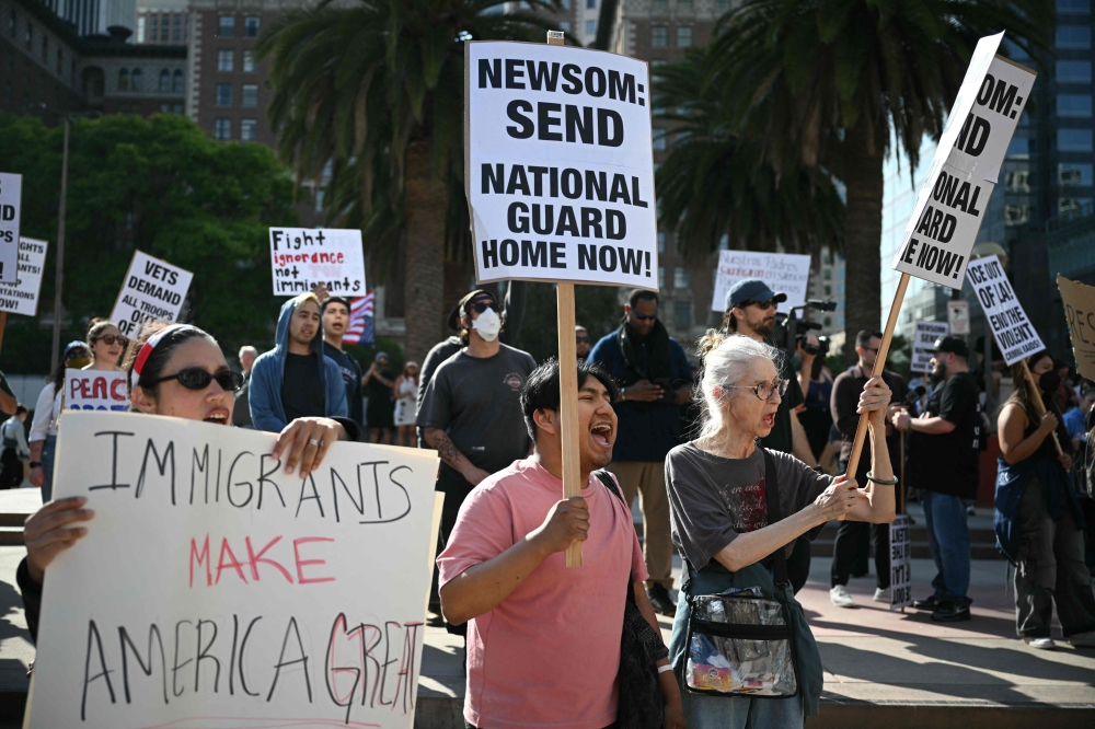 Protesters hold signs during a protest against federal immigration operations at Pershing Square in downtown Los Angeles yesterday. — AFP pic