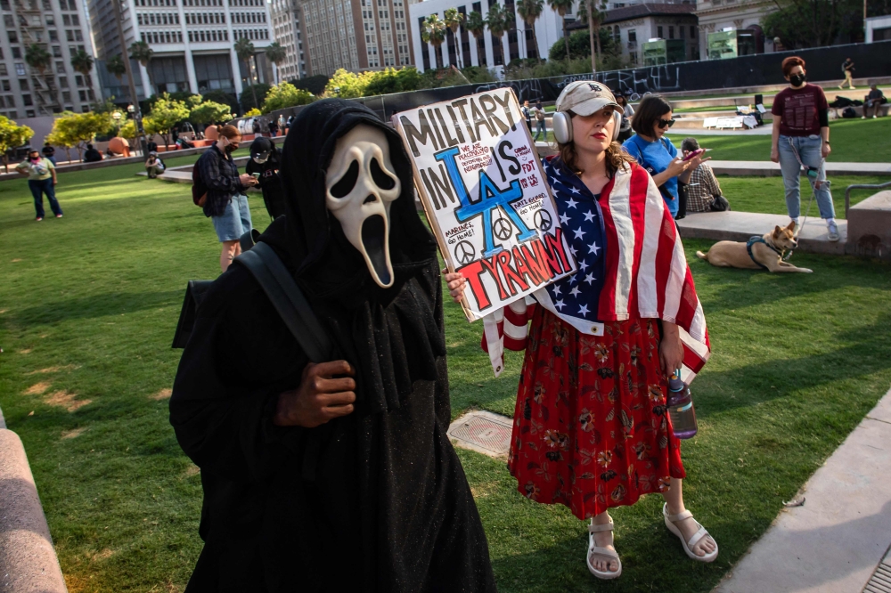 A person wears a 'Ghostface' mask next to another holding a sign as they gather at Pershing Square to protest against federal immigration operations in downtown Los Angeles yesterday. — AFP pic