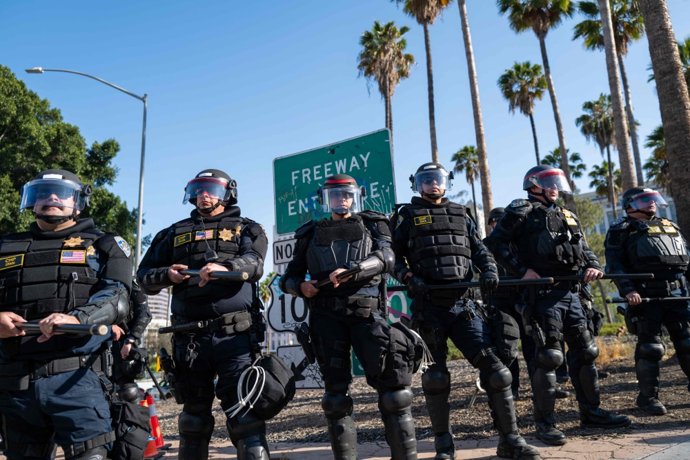 Police stand on guard as protesters march through downtown Los Angeles as demonstrations continue after a series of immigration raids began last Friday. — AFP pic