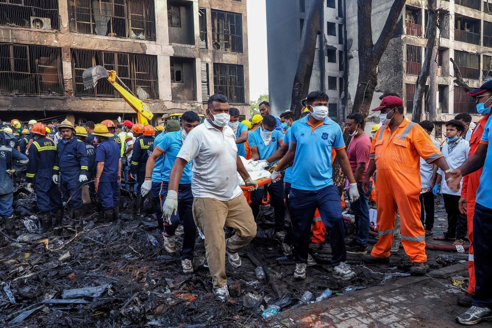 Rescue officials carry a victim's body at the site where Air India flight 171 crashed in a residential area near the airport in Ahmedabad yesterday. — AFP pic