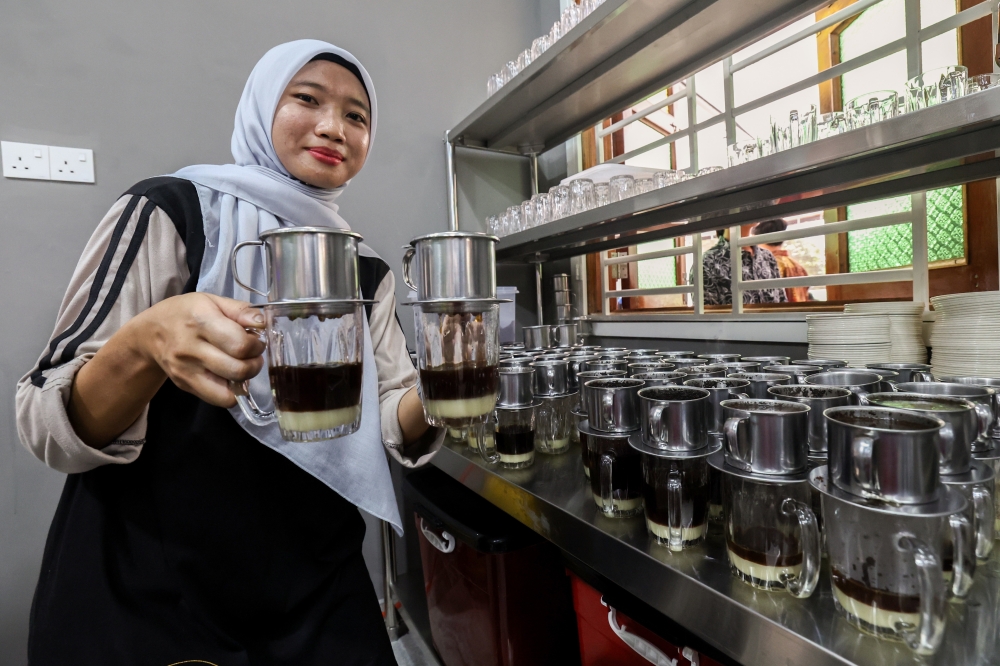 Ainun Hajar Kamaruddin holds a glass of freshly brewed Kopi Tenggek at the new Kopi Tenggek Tanjung Piai outlet in Larkin June 15, 2025. — Bernama pic