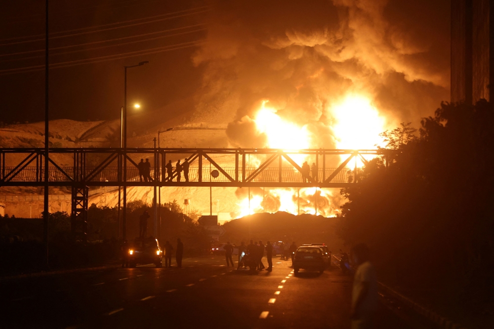 People watch from a bridge as flames from an Israeli attack rise from Sharan Oil depot, following Israeli strikes in Tehran June 15, 2025. — Reuters pic