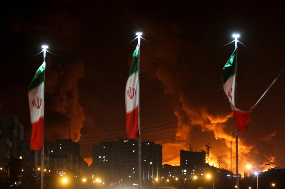 Iranian flags fly as fire and smoke from an Israeli attack on Sharan Oil depot rise, following Israeli strikes on Iran, in Tehran, Iran, June 15, 2025. — Reuters pic