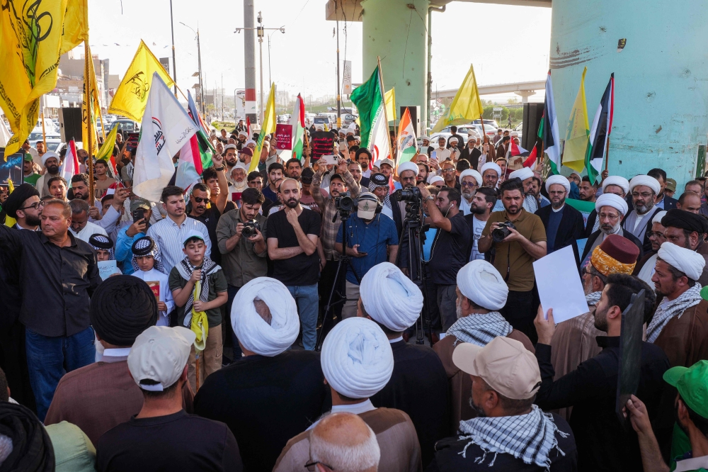 Iraqi protesters including clerics and tribal leaders lift placards and flags during a rally in support of Iran against the US and Israel in Iraq's Shiite holy city of Najaf yesterday. — AFP pic