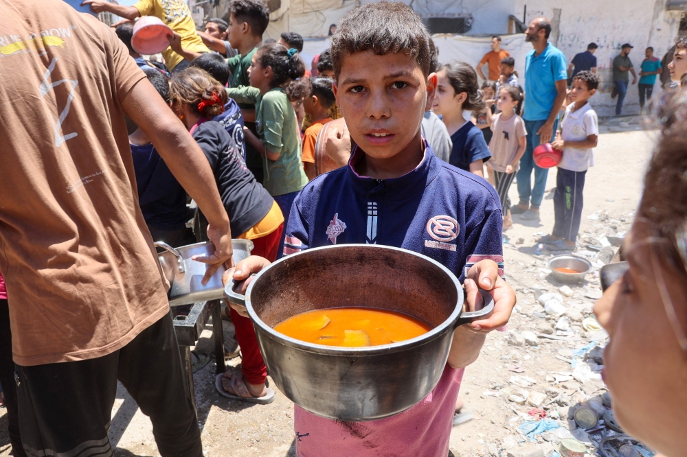 A Palestinian boy carries a pot with food collected at a charity kitchen providing hot meals in Rimal neighbourhood in Gaza City June 18, 2025. — AFP pic