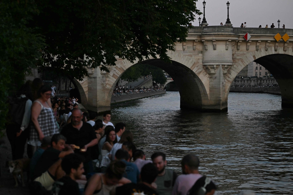 Visitors sit as the sun sets on the docks of the Seine river near the Square du Vert-Galant with the Pont Neuf in the background, in Paris, on Wednesday. — AFP pic