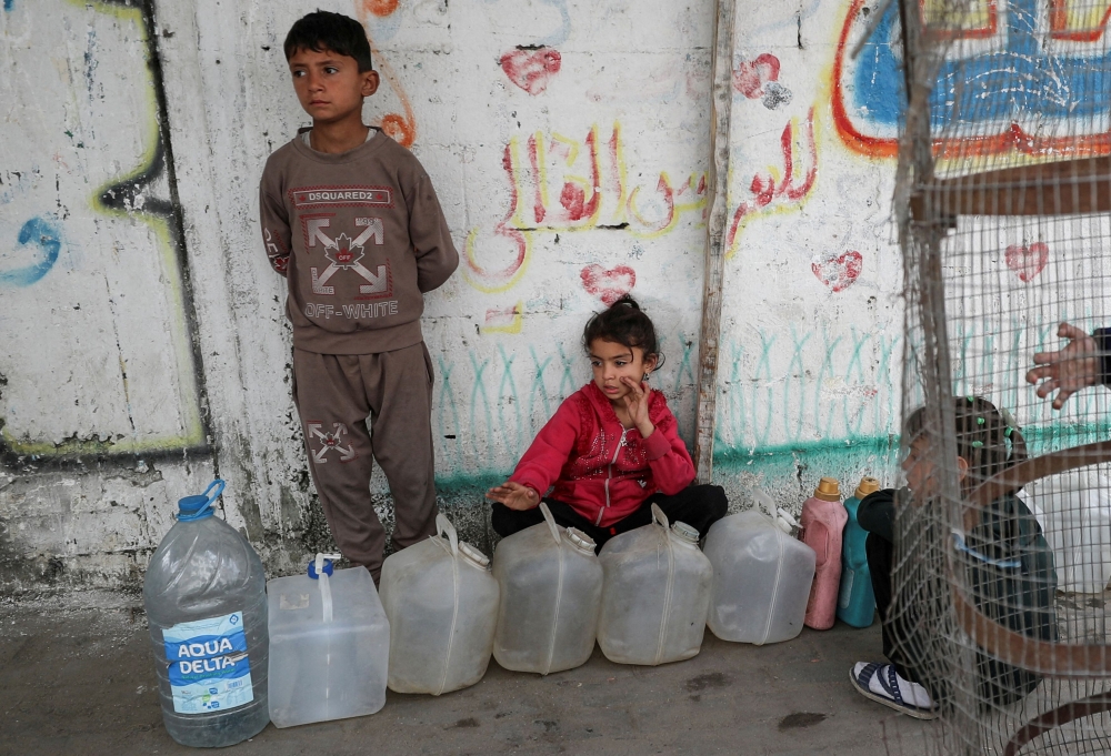 Palestinian children gather near containers used for water, in Gaza City April 6, 2025. — Reuters pic 