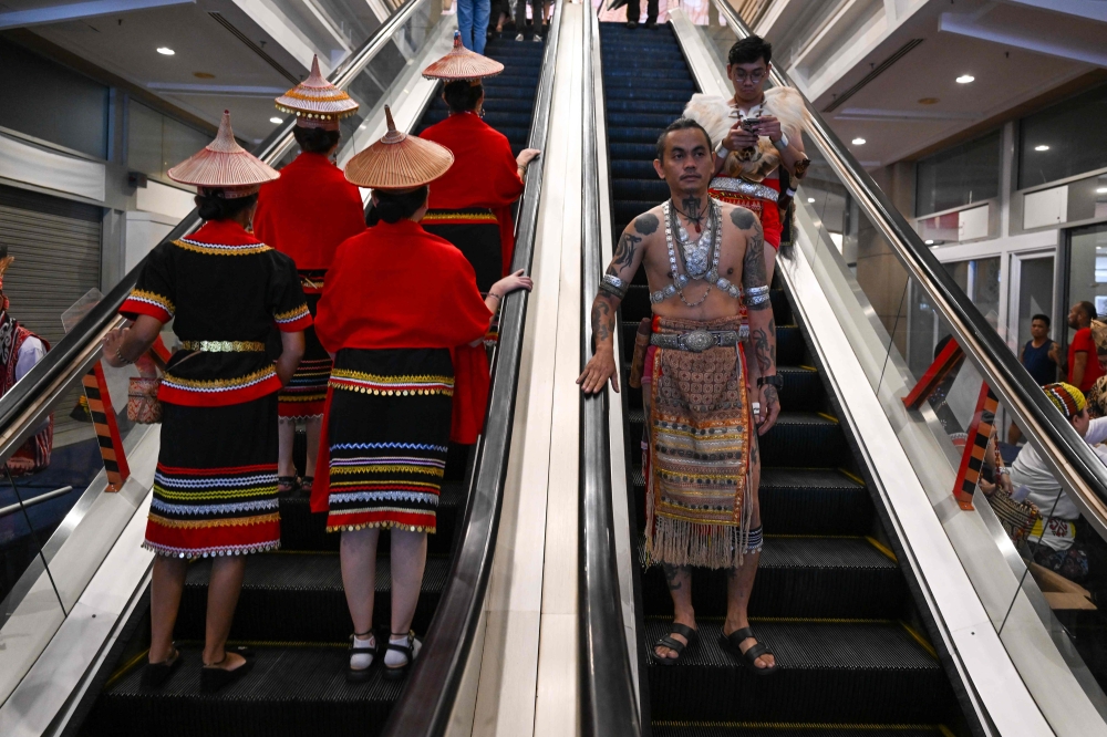 Indigenous Bidayuh (left) and Iban (right) natives in their respective traditional garments ride escalators inside a mall during the Gawai Dayak Culture Parade in Kuching, Sarawak, on June 21, 2025.— AFP pic