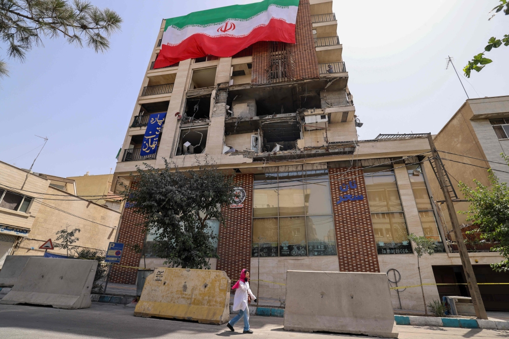 A woman walks past a residential building that was hit in an Israeli strike covered with a big Iranian flag, in Tehran on June 25, 2025. — AFP pic