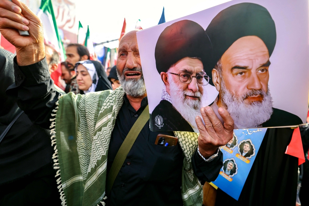 A man holds portraits of Iran’s supreme leader Ayatollah Ali Khamenei (right) and the late supreme leader Ayatollah Ruhollah Khomeini, during the funeral procession of military commanders and scientists killed during Israeli strikes, in Tehran June 28, 2025. — AFP pic