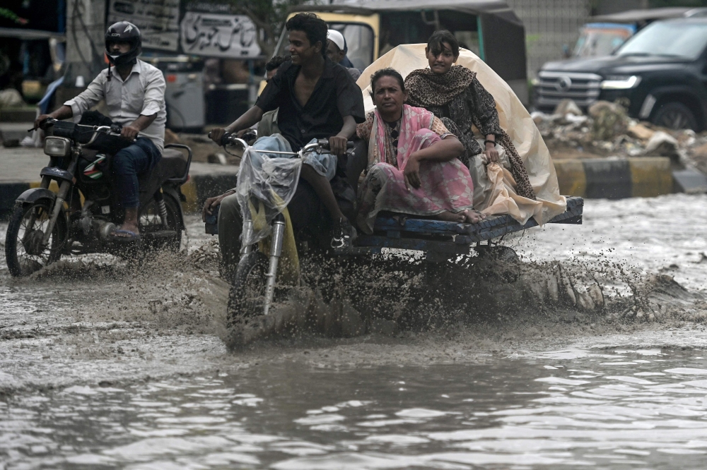 Commuters make their way through a flooded street after heavy rainfall in Karachi on June 28, 2025. — AFP pic 