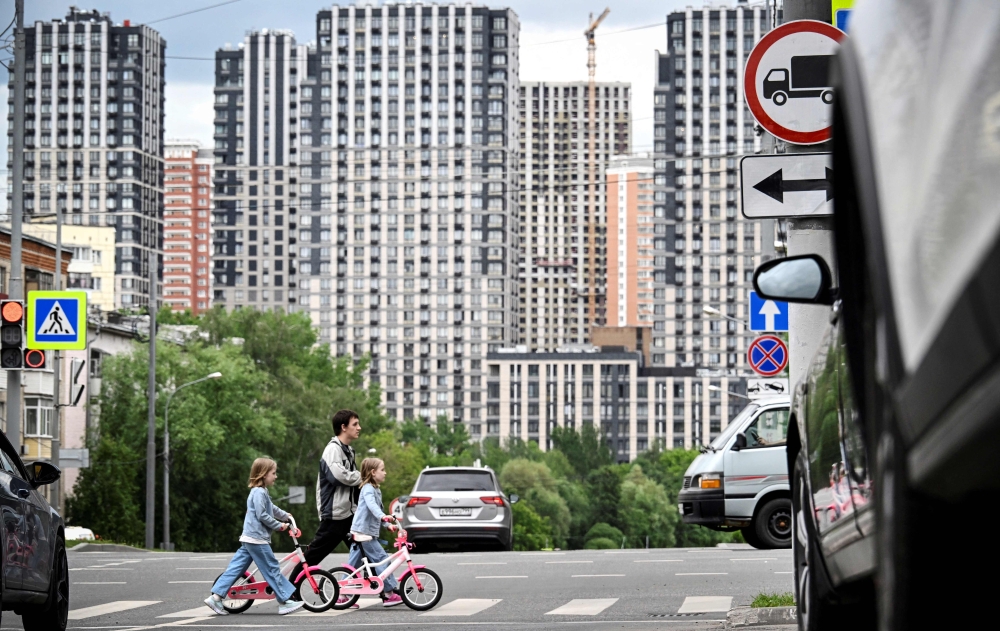 A family crosses a street in front of a newly built apartment buildings quarter in Moscow on June 11, 2025. — AFP pic