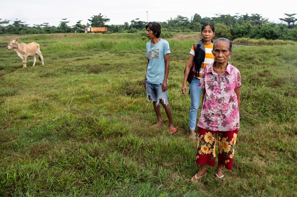 In this photo taken on May 24, 2025, Moharen Tambiling (L), his sister Alayma (C) and their mother stand on their coconut and rice farms next to stockpiled nickel ore at Maasin village in Brooke's Point, Palawan province. — AFP pic