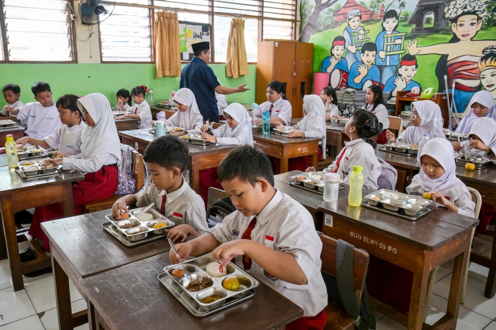 Elementary schoolchildren eating food prepared by the government's free meal program at a classroom in Jakarta. — AFP pic