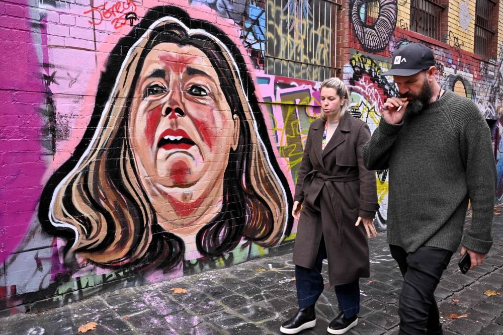 This photo taken on June 17, 2025 shows people in a Melbourne laneway walking past a mural by street artist Jarrod Grech of Erin Patterson, an Australian woman accused of murdering three members of her husband's family with a toxic mushroom-laced beef Wellington lunch. — AFP pic