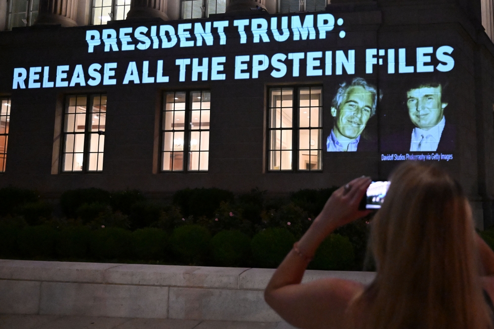 A person takes a photo as a message calling on President Donald Trump to release all files related to Jeffrey Epstein is projected onto the US Chamber of Commerce building across from the White House in Washington, DC July 18, 2025. — AFP pic