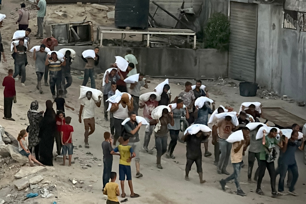 Men walk carrying sacks of flour after raiding a truck carrying foodstuffs in Khan Yunis, in the southern Gaza Strip yesterday. — AFP pic