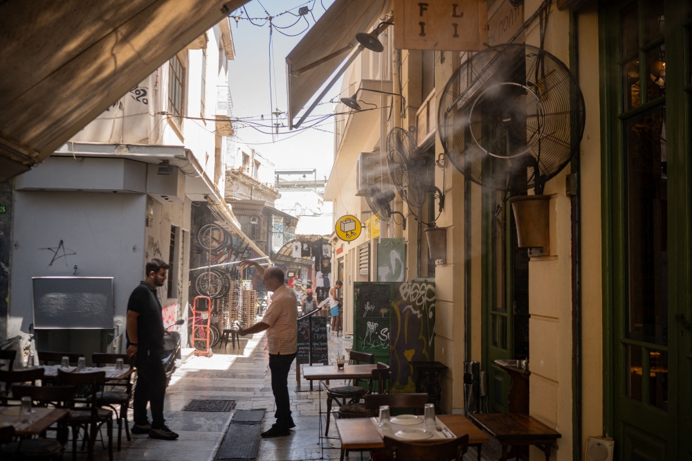 Restaurant employees chat near a misting machine spraying water, during a heatwave, in Athens July 24, 2025. — AFP pic