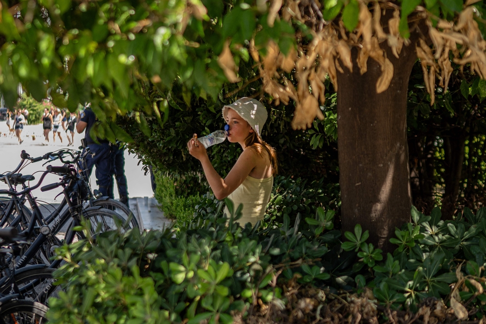 A girl sits in the shade as she drinks water outside of the Greek Parliament, during a heatwave, in Athens July 24, 2025. — AFP pic