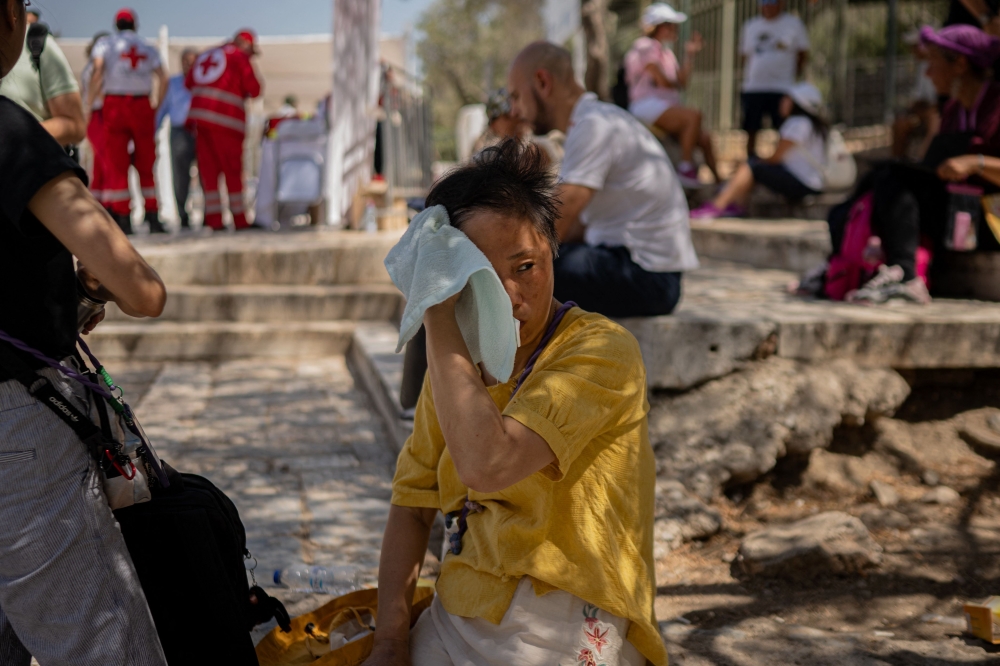 A tourist wipes her face with a towel outside of the closed Acropolis Hill monument site in Athens July 23, 2025. — AFP pic