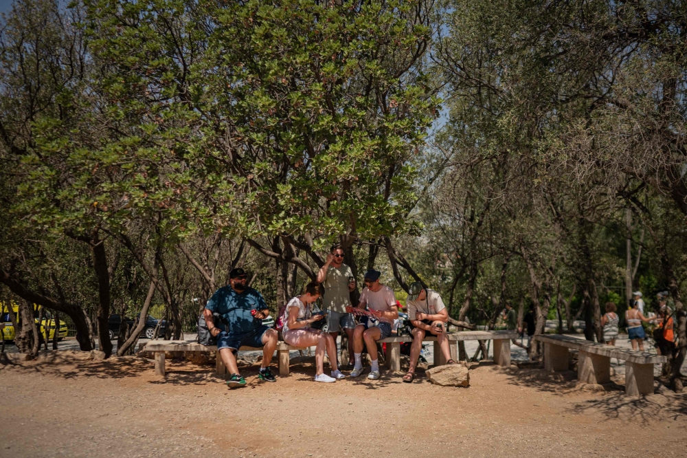 Tourists sit in the shade outside of the closed Acropolis Hill monument site in Athens July 23, 2025. — AFP pic