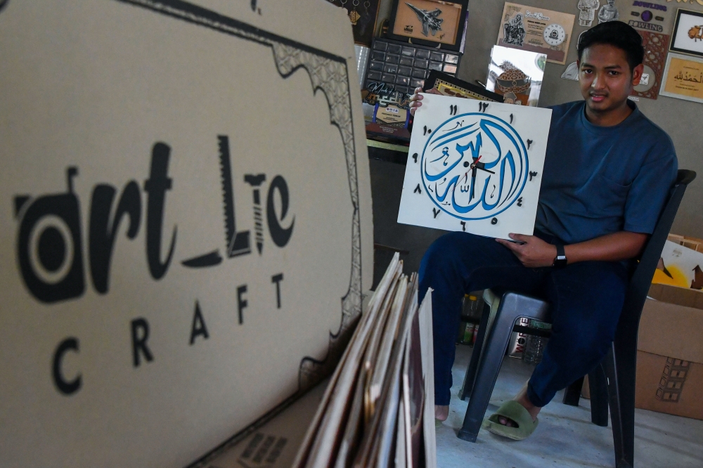 Muhammad Ali Che Pa shows some of his laser-engraved woodcrafts at his workshop in Kampung Pangkal Kalong, Kok Lanas. — Bernama pic