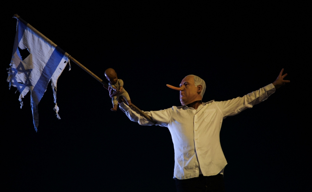 A demonstrator wearing a fake nose and a mask of Israeli Prime Minister Benjamin Netanyahu, holds a baby doll and a torn Israeli flag, while taking part in a protest demanding an end to the war in Gaza and the release of all hostages, in Tel Aviv July 24, 2025. — Reuters pic