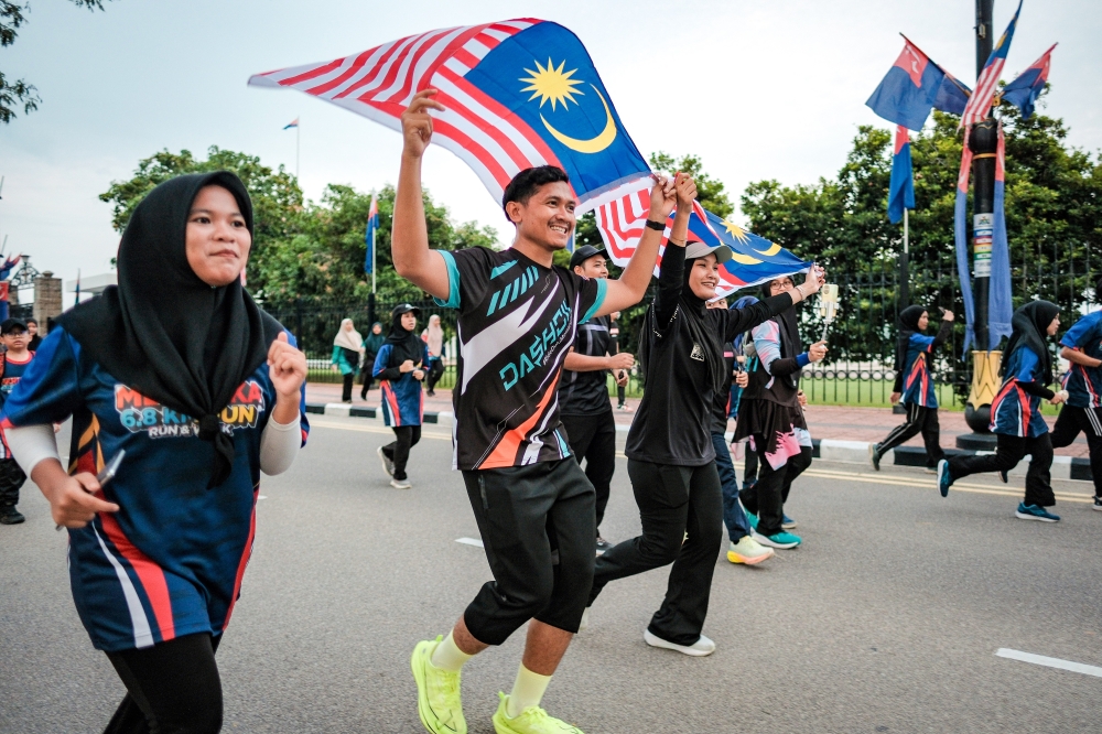 Participants ran while waving the Jalur Gemilang during the Merdeka 6.8KM Fun Run & Walk, officiated by Communications Minister Datuk Fahmi Fadzil in conjunction with the Launch of the National Month and Fly the Jalur Gemilang 2025 campaign at Dataran Tanjung Emas in Muar. — Bernama pic