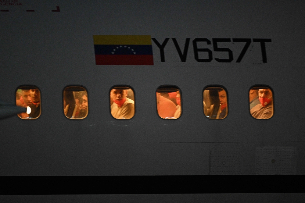 Venezuelan migrants who were jailed in El Salvador peer out the windows of the plane as it lands at Simon Bolivar International Airport in Maiquetia, Venezuela, July 18, 2025. — AFP pic