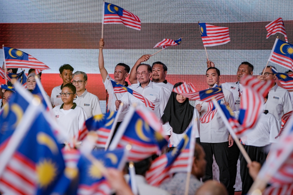 Prime Minister Datuk Seri Anwar Ibrahim (right) sings the Jalur Gemilang anthem while waving the national flag during the Launch Ceremony of the National Month and Fly the Jalur Gemilang 2025 campaign at Dataran Tanjung Emas in Muar. — Bernama pic