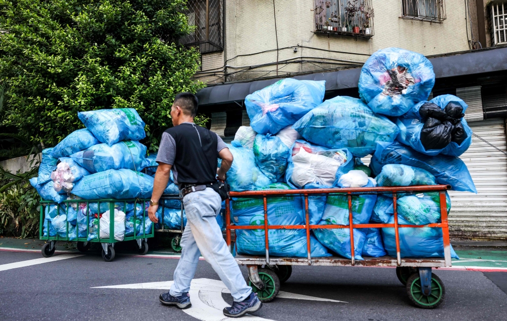 This photo taken on June 19, 2025 shows a man taking a cart loaded with trash to a garbage truck in Taipei. Taiwanese residents holding plastic bags of rubbish stand on a footpath as a yellow garbage truck playing classical music over a loudspeaker pulls up. — AFP pic