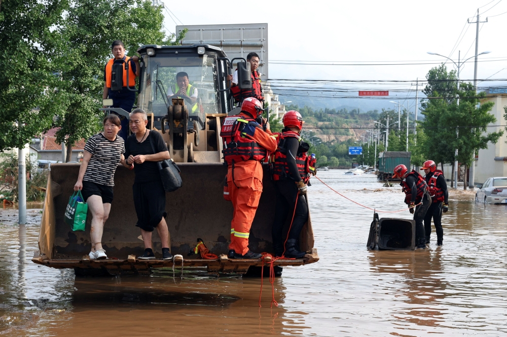 Rescue workers set up a barrier to cover a manhole in the middle of a flooded road, near a front loader carrying rescuers and stranded residents following heavy rainfall in Miyun district of Beijing, China July 28, 2025. — Reuters pic 