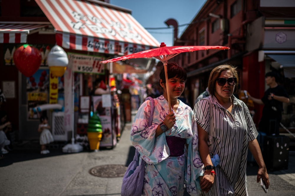 Tourists share a traditional umbrella to shelter from the sun while walking along a shopping street at the Asakusa district near Sensoji Temple, on a hot day in Tokyo on July 28, 2025. — AFP pic
