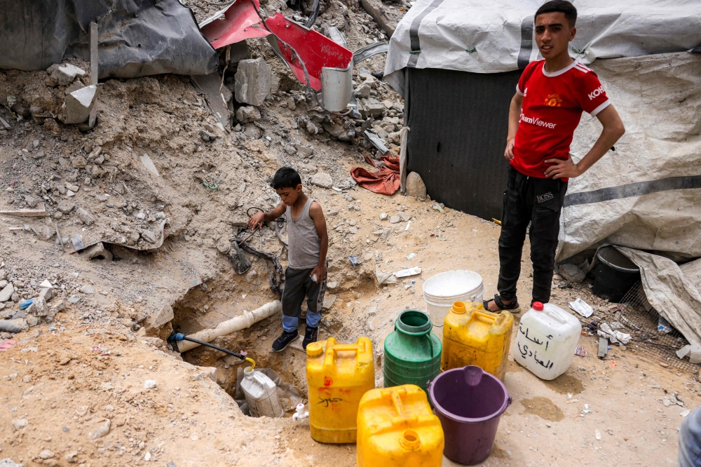 A boy fills up containers with water from the remaining water still left in underground pipes, in Beit Lahia in the northern Gaza Strip on April 24, 2025. — AFP pic