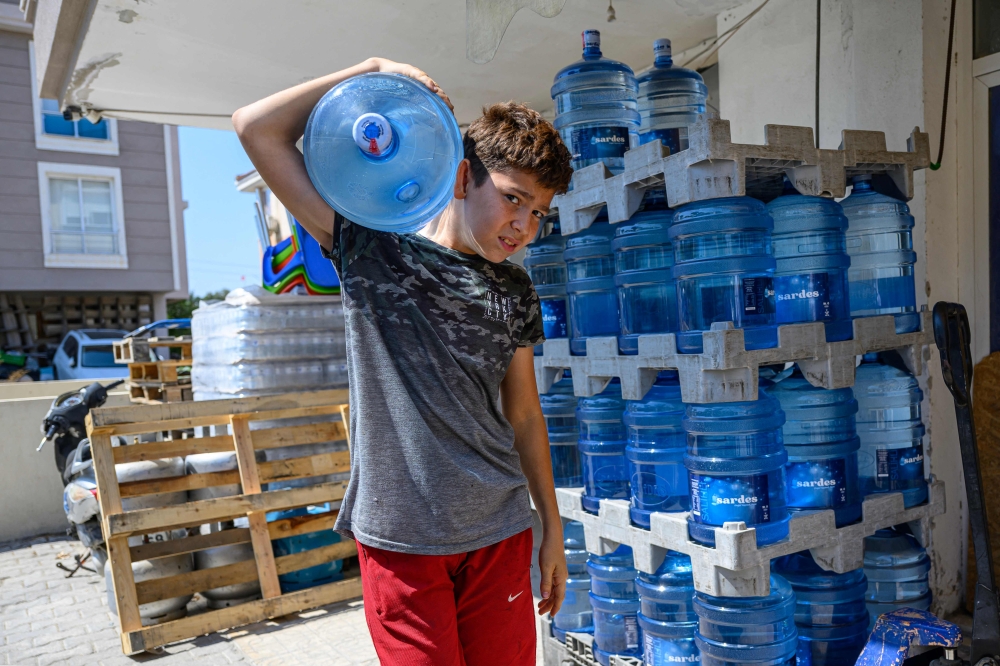 A young boy comes out of a store carrying a barrel of drinking water in the Turkey west province of Izmir, on July 31, 2025. — AFP pic