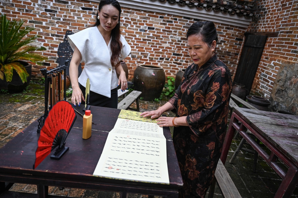 The photo taken on July 21, 2025 shows ‘Nushu’ inheritor He Yuejuan (right) displaying a ‘Nushu’ calligraphy work at her workshop at Goulan Yao Village in Jiangyong county, southern China’s Hunan province. — AFP pic 