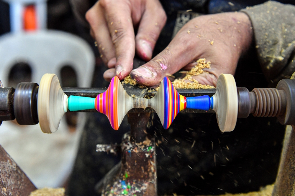Helmi Naim puts the finishing touches on wooden spinning tops produced at his workshop. — Bernama pic 