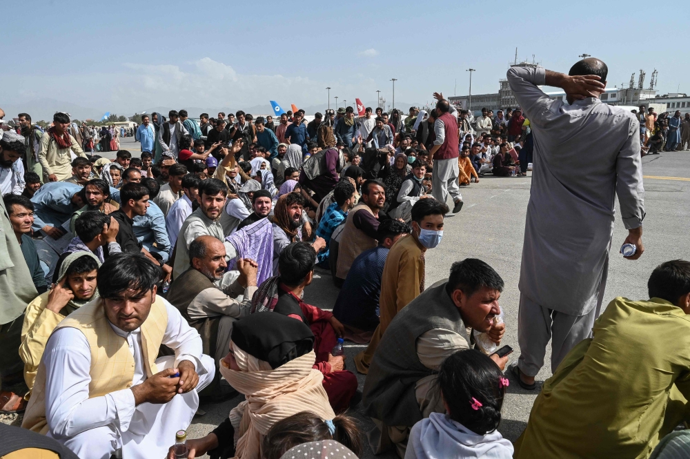 Afghan passengers sit as they wait to leave the Kabul airport in Kabul on August 16, 2021, after a stunningly swift end to Afghanistan's 20-year war, as thousands of people mobbed the city's airport trying to flee the group's feared hardline brand of Islamist rule. — AFP pic
